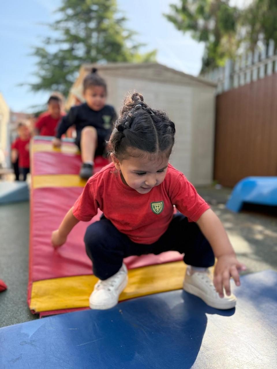 A child leaps between soft play mats during an outdoor obstacle activity.