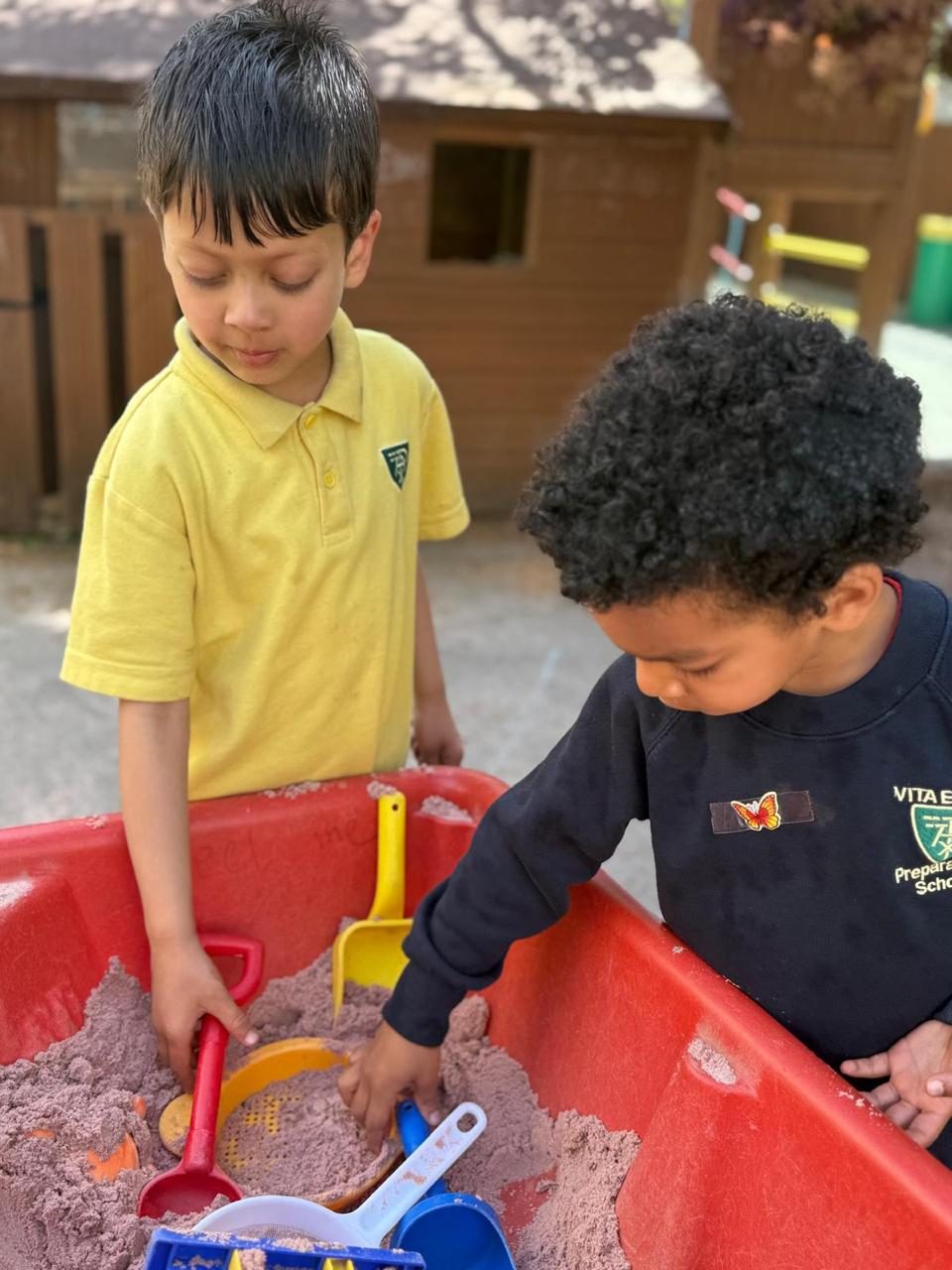 Two nursery children explore the sand tray side by side.