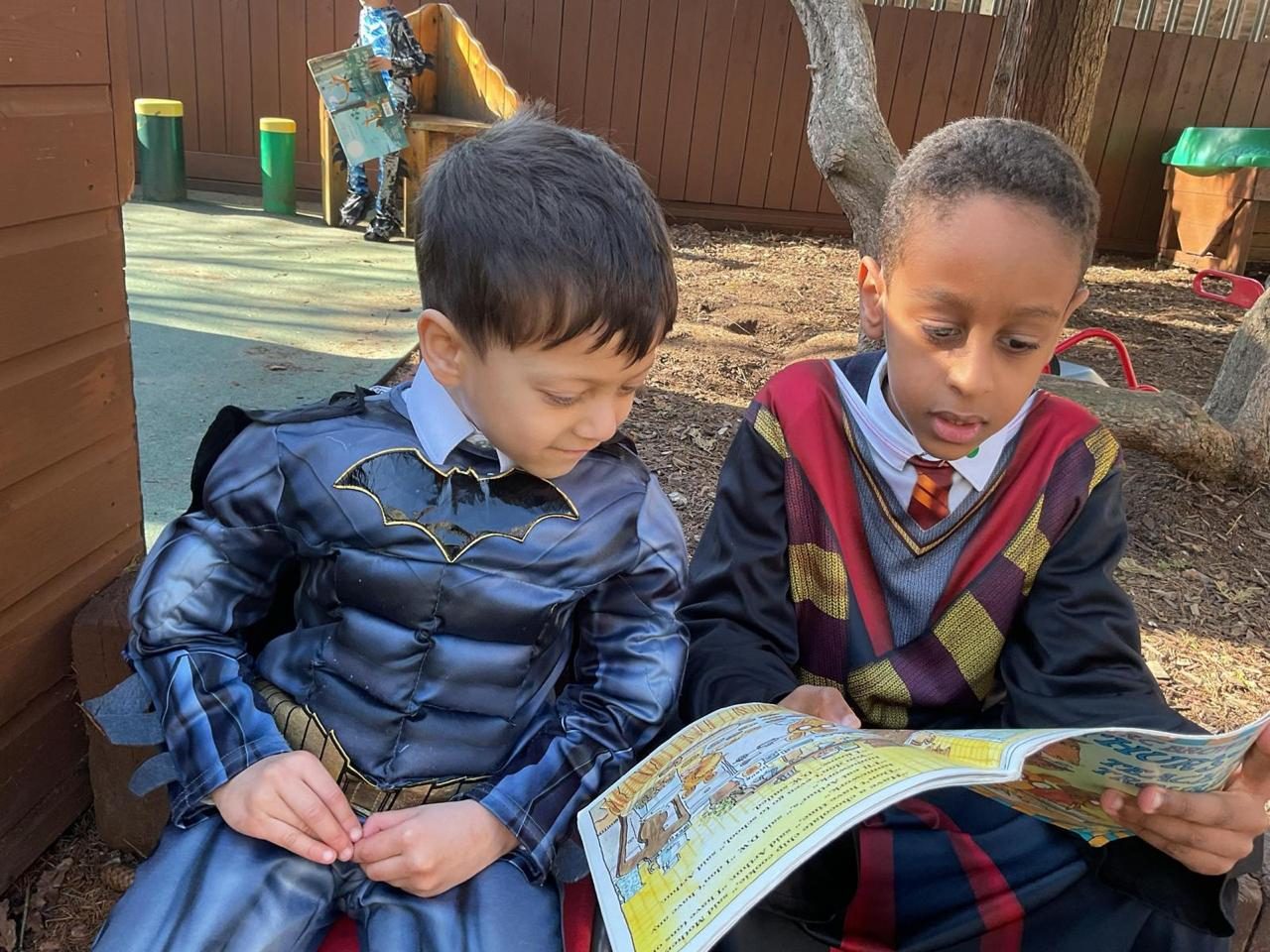 Two children in World Book Day costumes read together on the carpet.