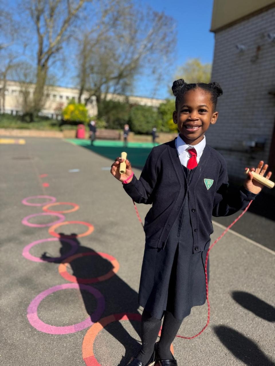 A smiling child skips with a rope in the playground.