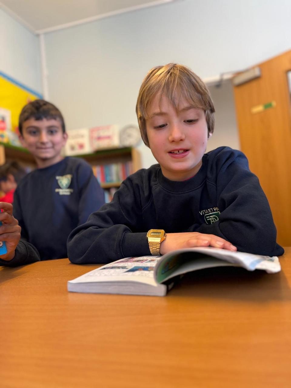 Two pupils share a reading book at their classroom desk.